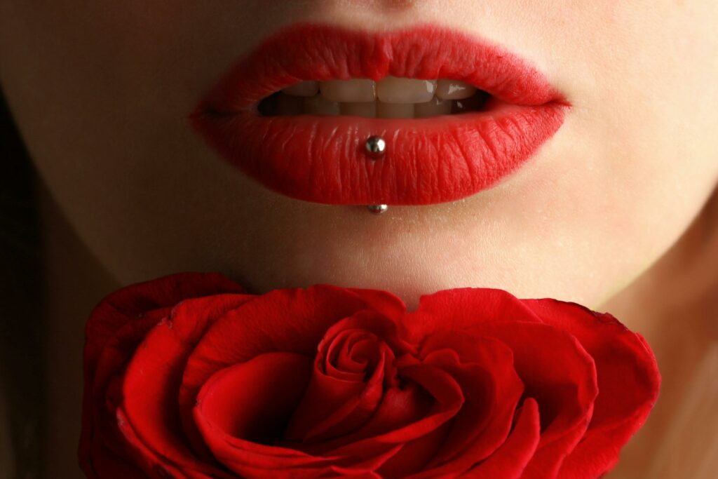 About Aesthetic close-up featuring red lipstick, lip piercing, and a red rose.